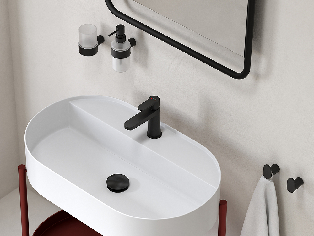 Łazienka z owalną, białą umywalką nablatową z czarnym korkiem, czarną baterią umywalkową Ferro Nostris, czarno-przeźroczystym dozownikiem mydła i kubkiem na szczoteczki, lustrem w czarnej ramie, czarnymi wieszakami na ręczniki i białym ręcznikiem.